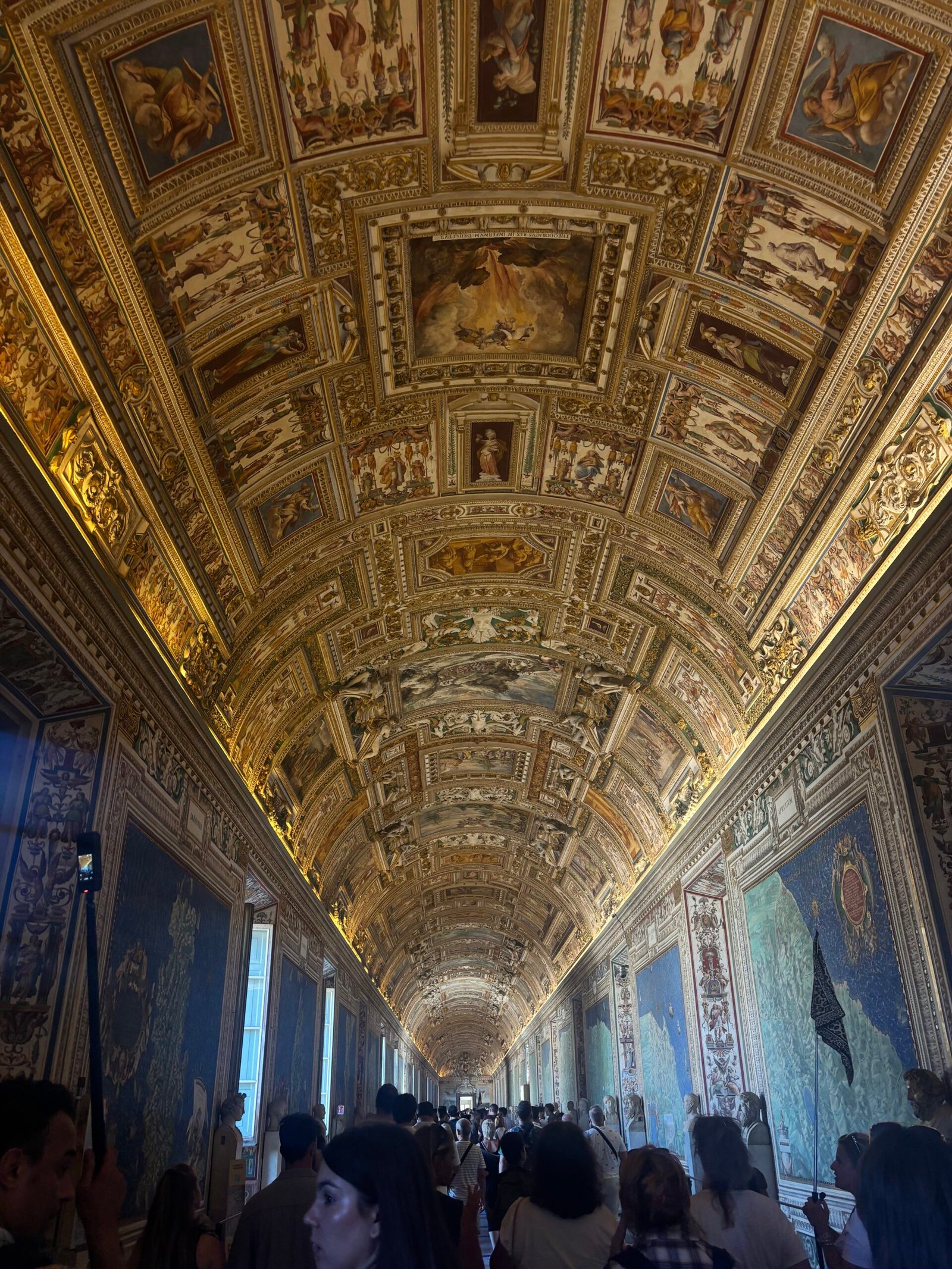 Rome, Italy — the ornately frescoed Gallery of Maps ceiling in the Vatican Museums, crowded with visitors
